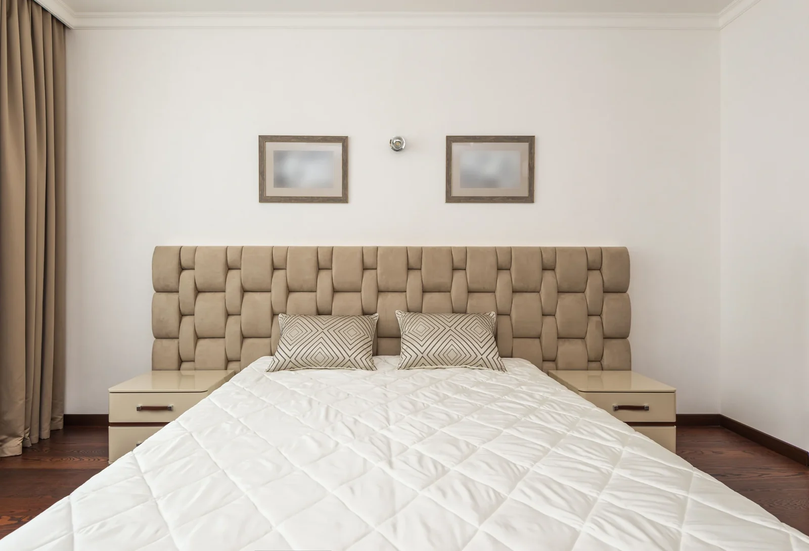 Beige bedroom with a quilted headboard, pillows and matching bedside furniture.