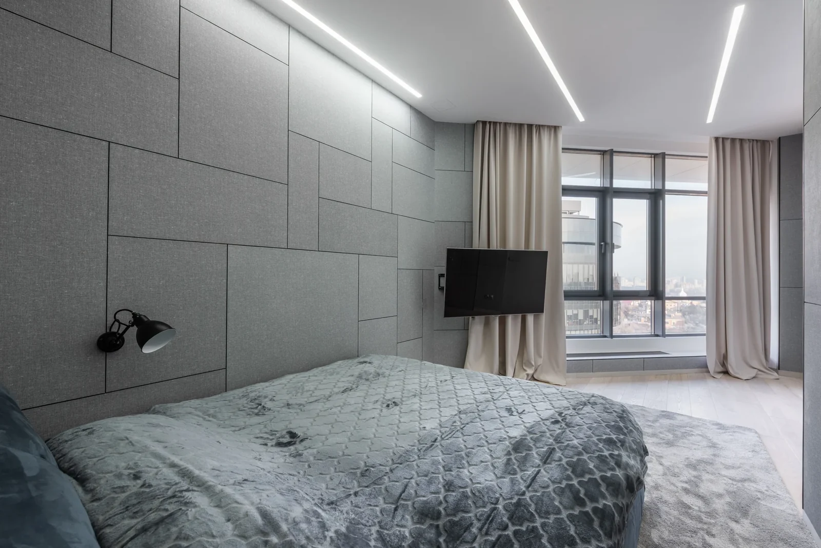 Modern bedroom with a bed on an area rug, a television and large curtained windows.