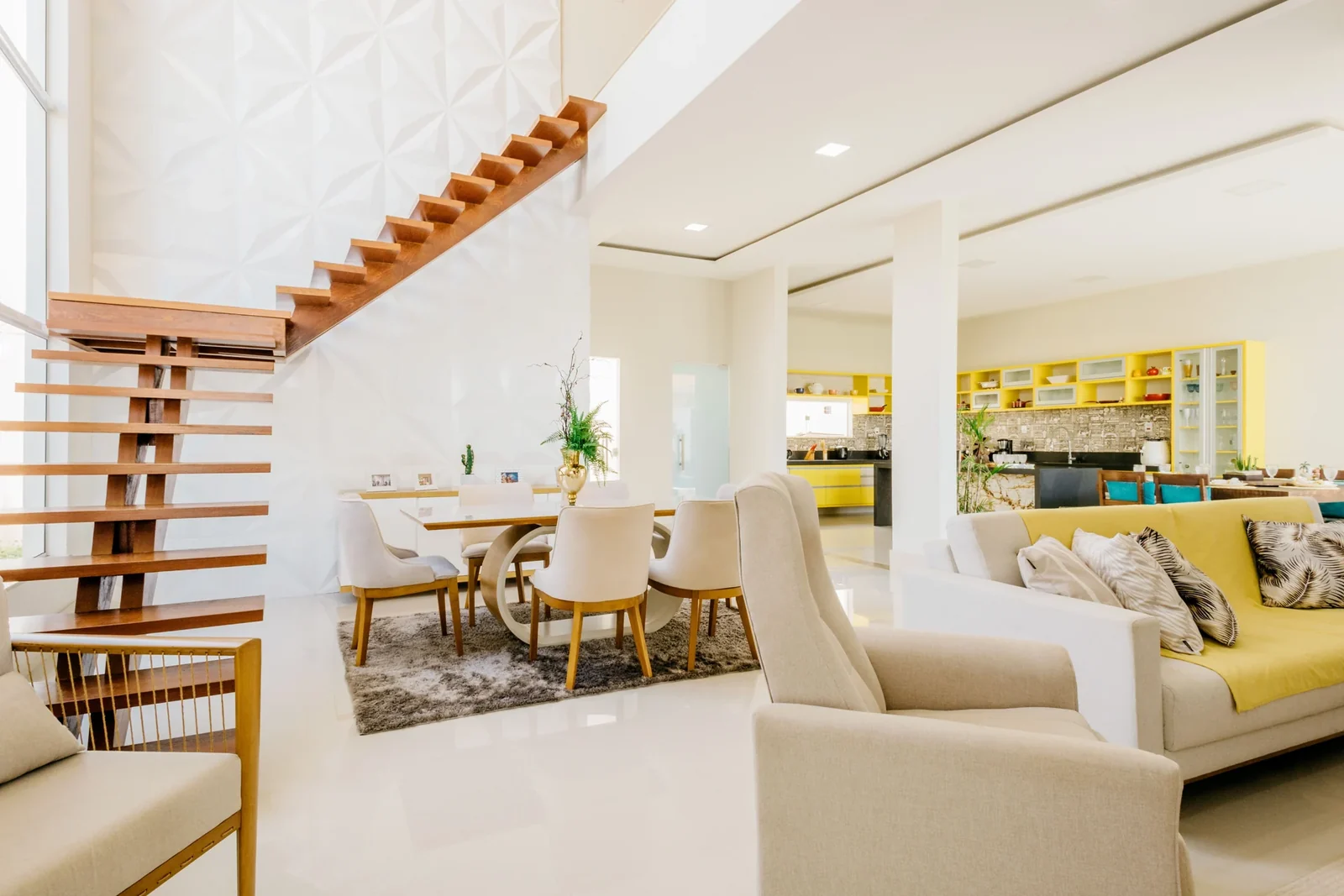 Open living space with a sofa, chairs, white walls, and a wooden staircase.