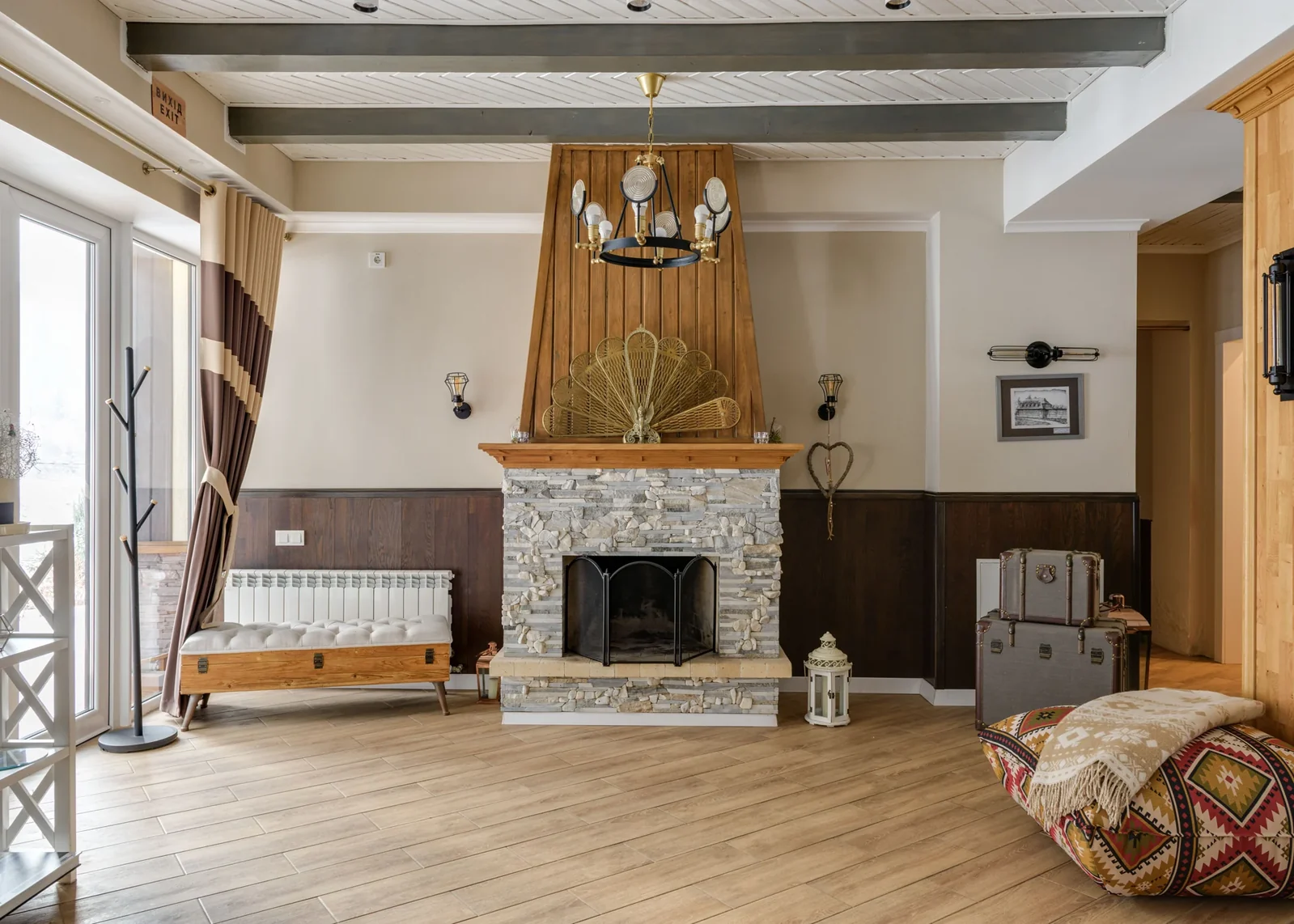 Living room with a stone fireplace, wood mantel, cream walls and exposed ceiling beams.