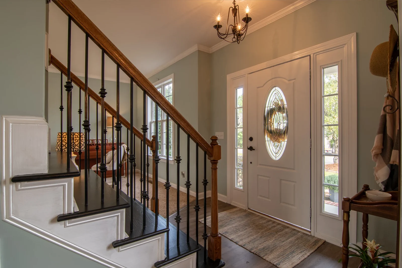 Home entry with a wood staircase, dark metal balusters, soft green walls and a white front door.