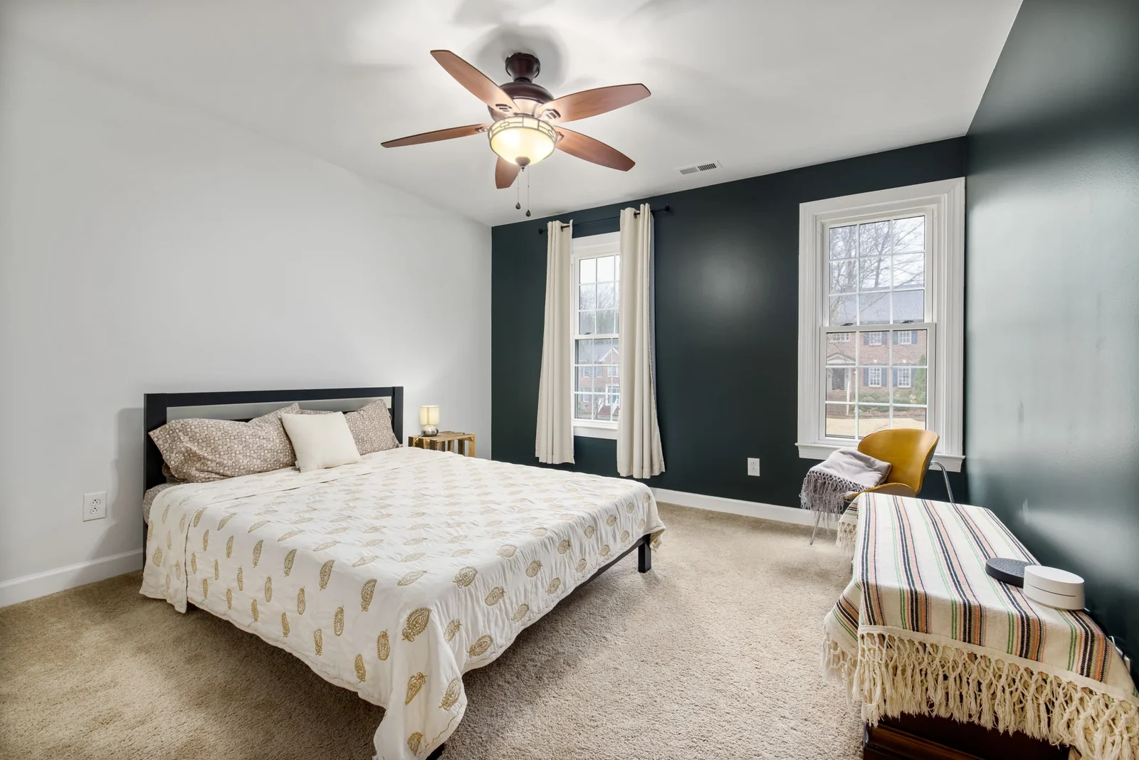 Bright bedroom with a large bed, carpeted floor, ceiling fan and windows.
