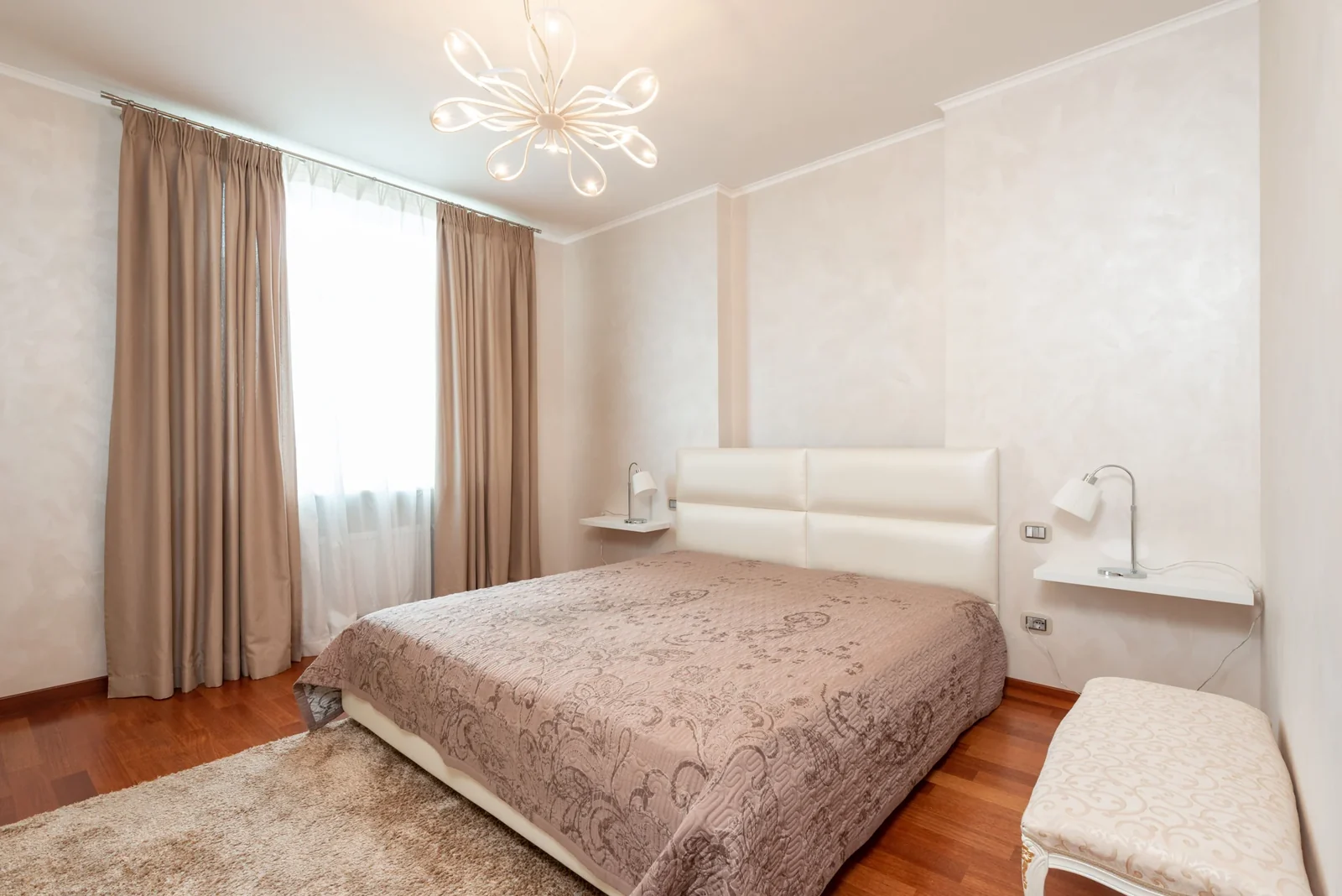 Neutral bedroom with a bed, upholstered bench, pendant lighting and a rug.