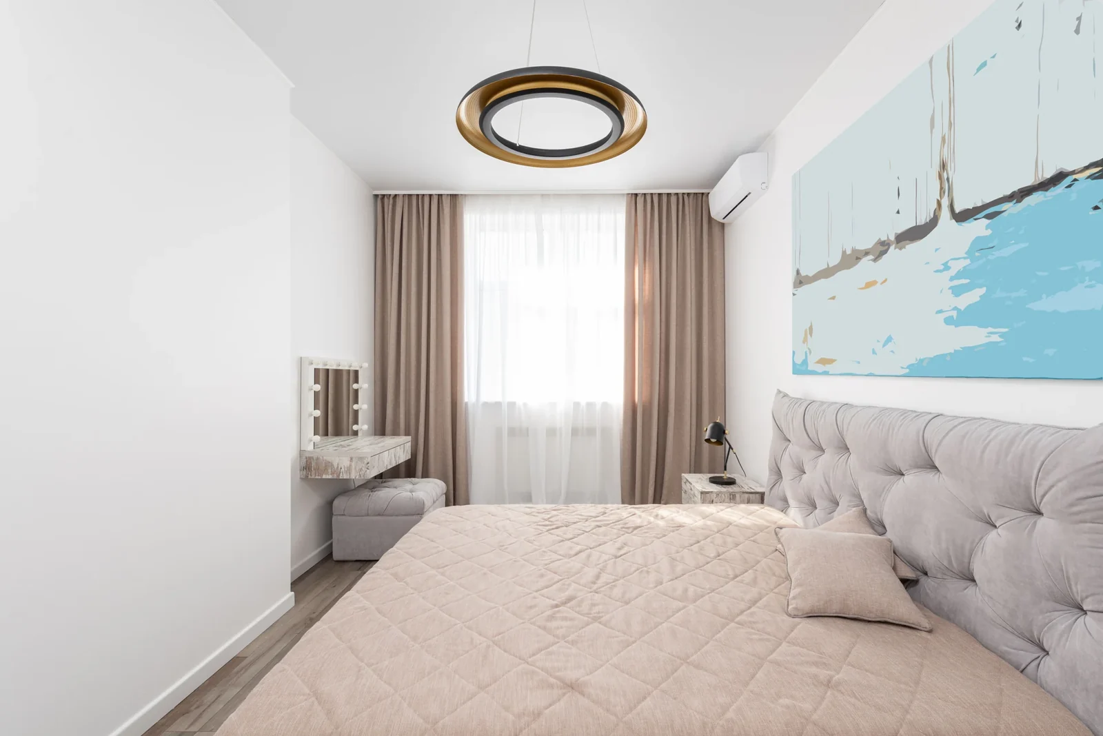 Modern bedroom with a beige bedspread, white walls and daylight through curtains.