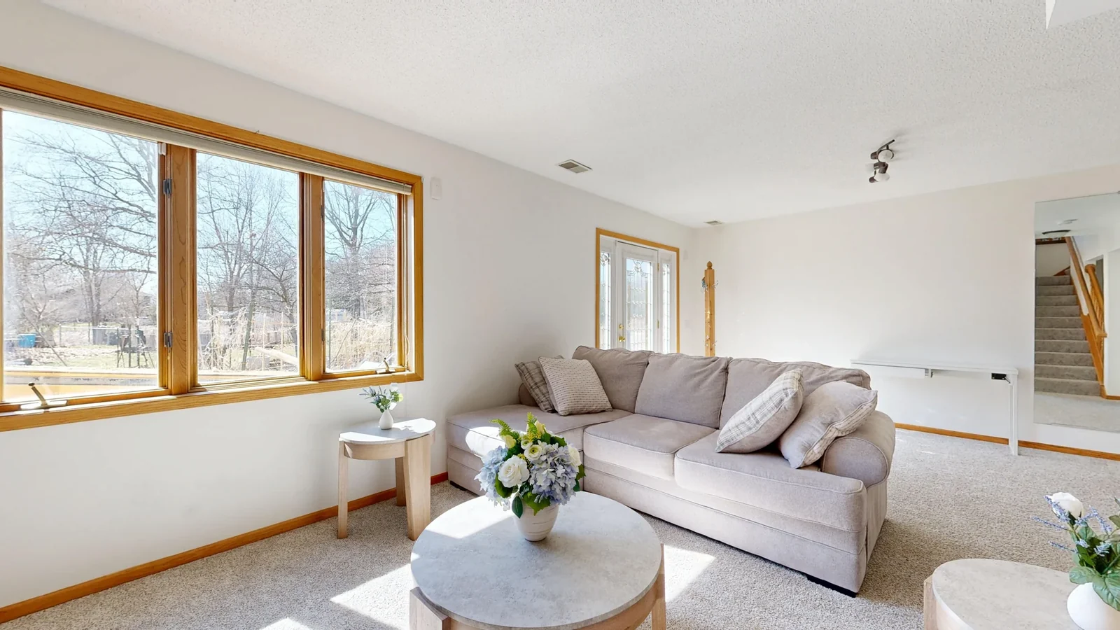 Living room with a beige sofa, wood-trimmed windows, and natural light.