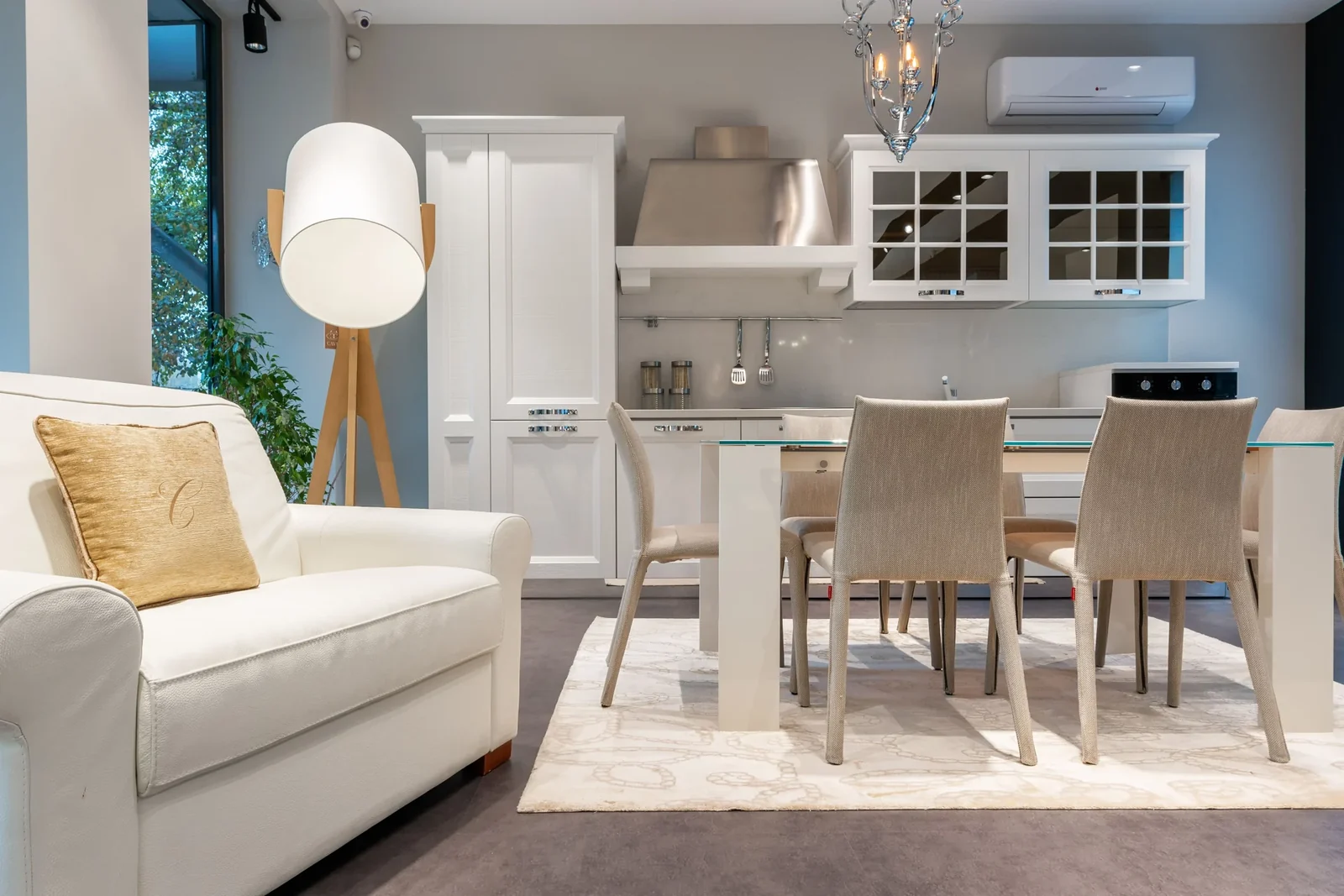 Neutral open interior with white upholstered seating, a dining table and kitchen cabinetry.