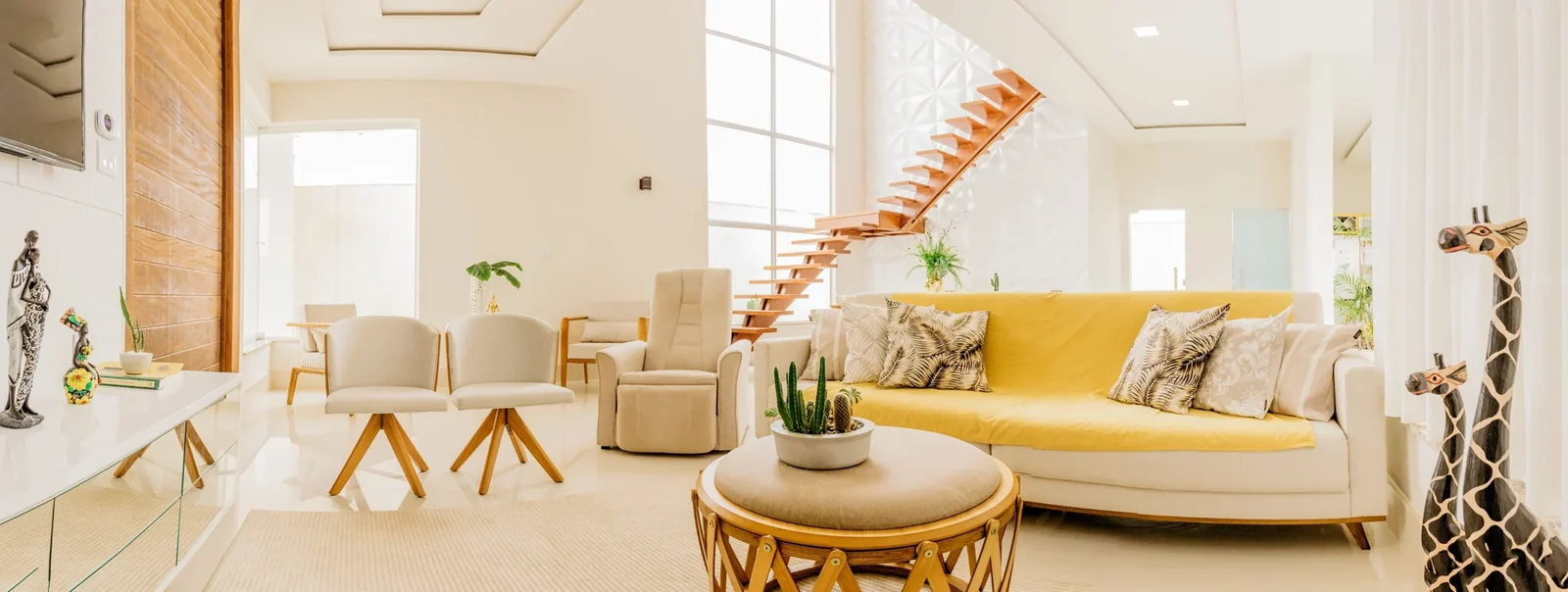 Bright living room with pale furniture, wooden details, and a staircase.