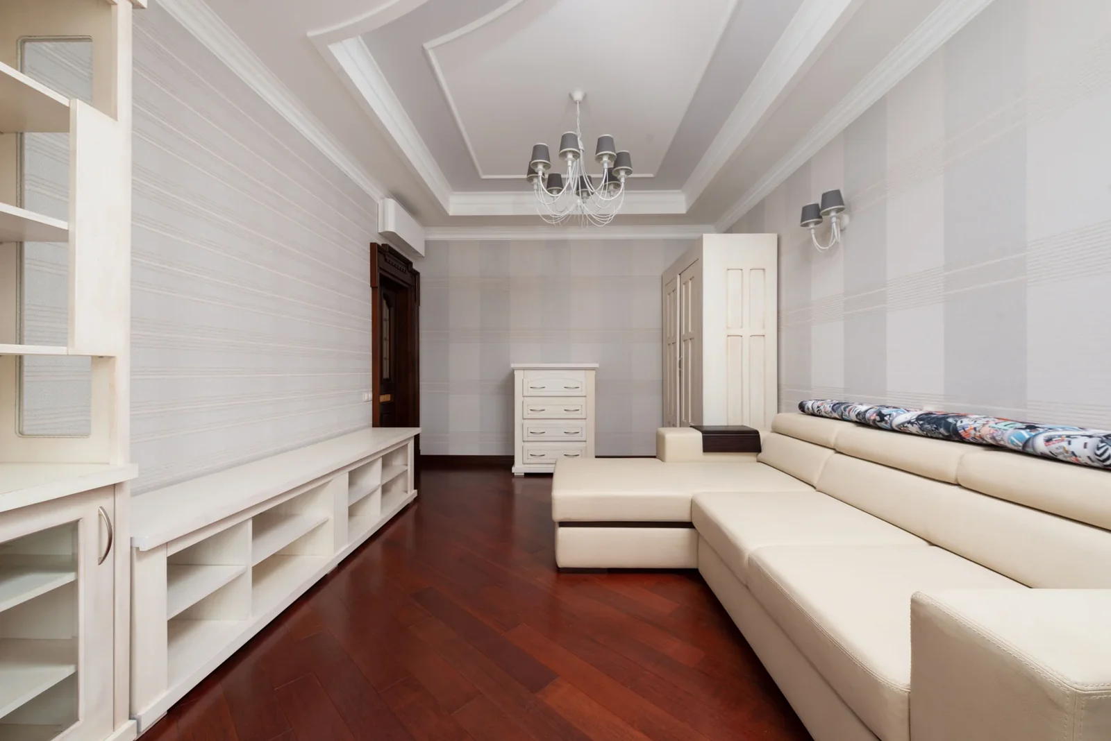 Spacious living room with a light sectional sofa, chandelier and wooden floor.