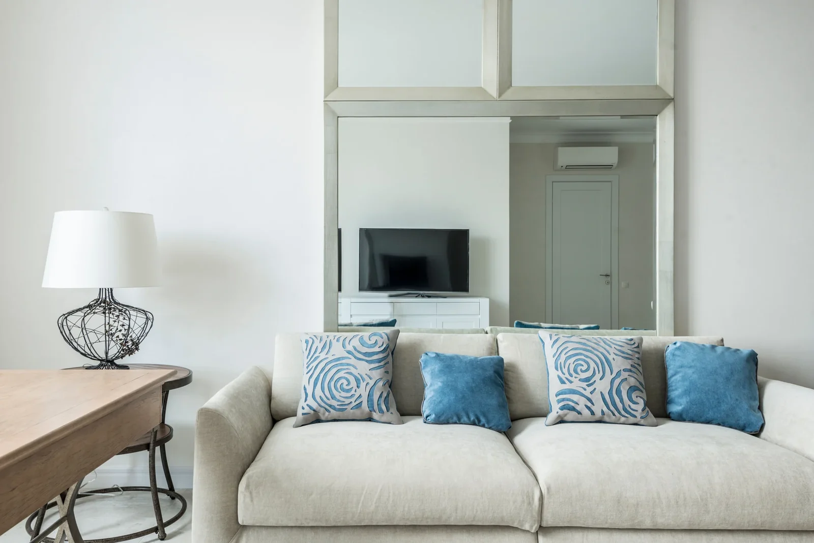Beige upholstered sofa with blue cushions beside a table lamp.