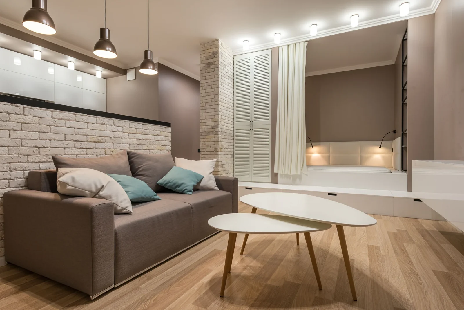 Living room with a beige sofa, white coffee table and pendant lights.