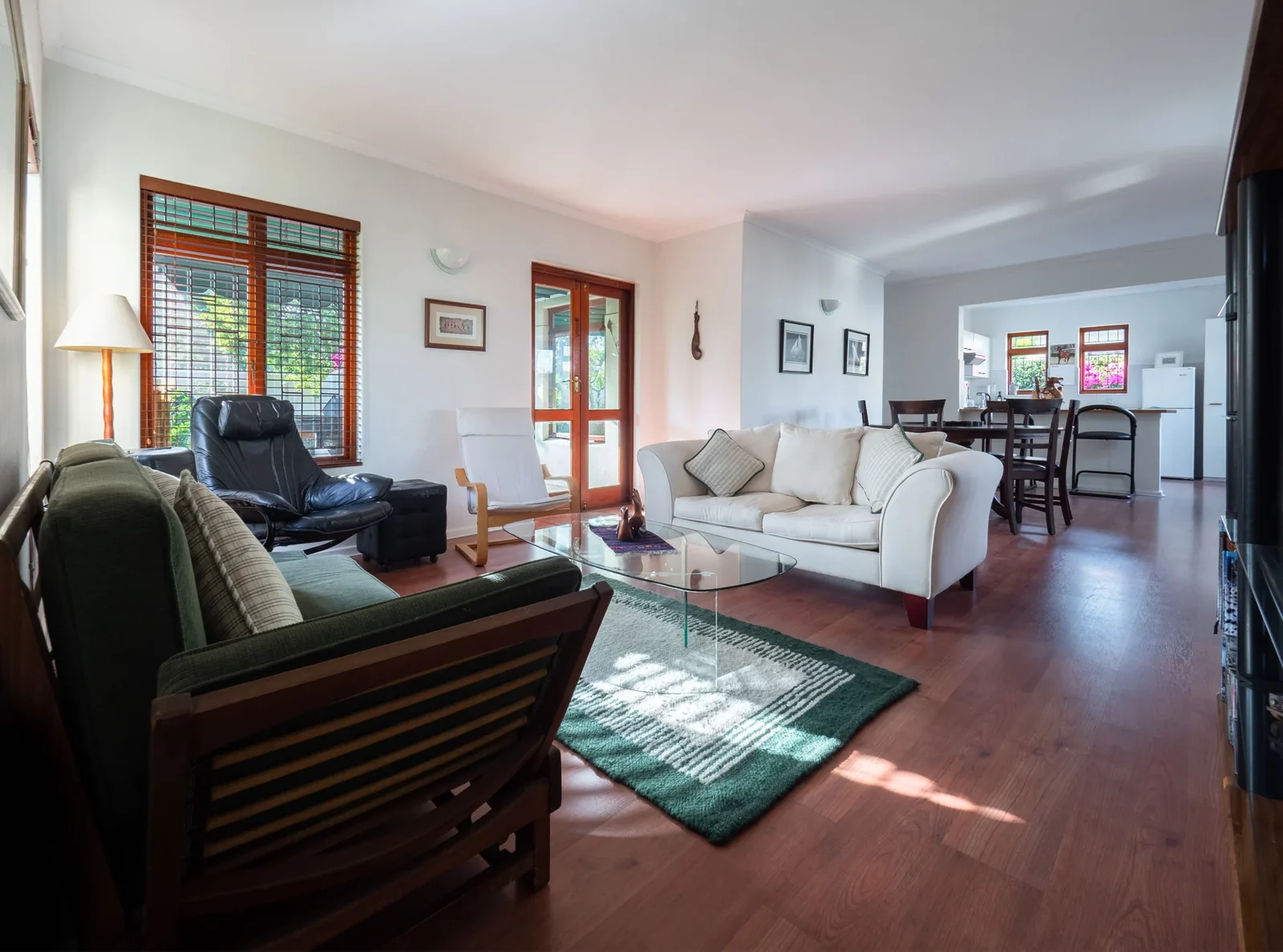Sunlit living room with cream and olive seating, a glass coffee table and wood flooring.