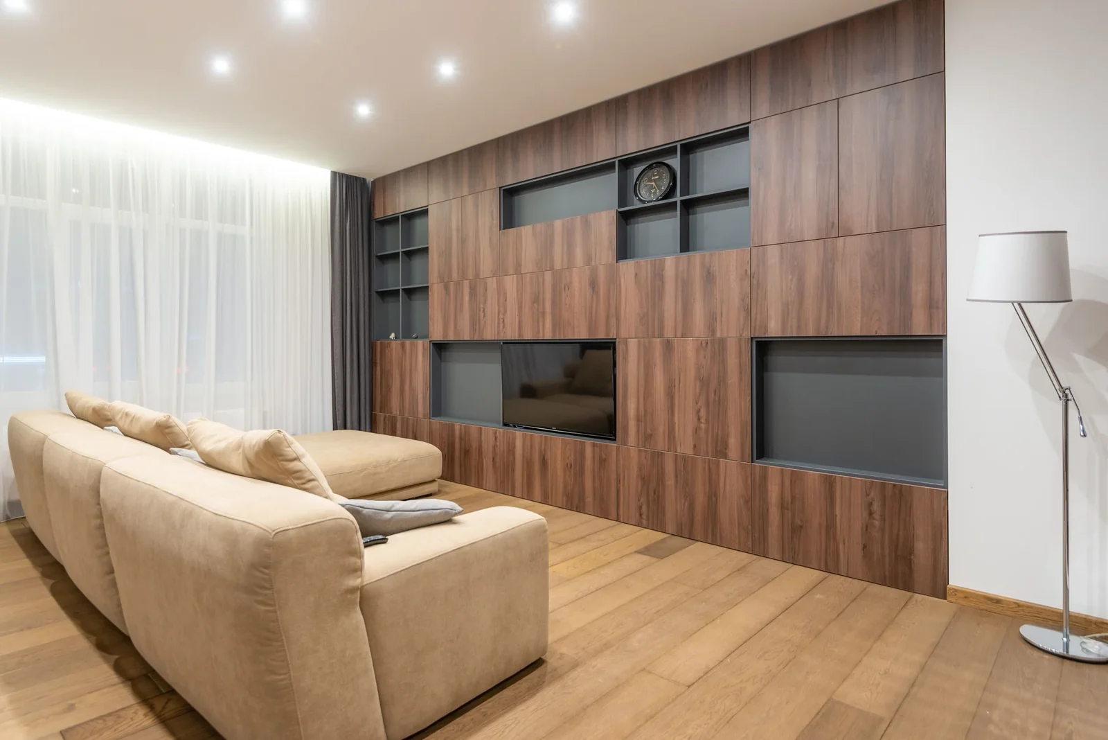 Neutral living room with a beige sofa, wood wall panels and shelves.