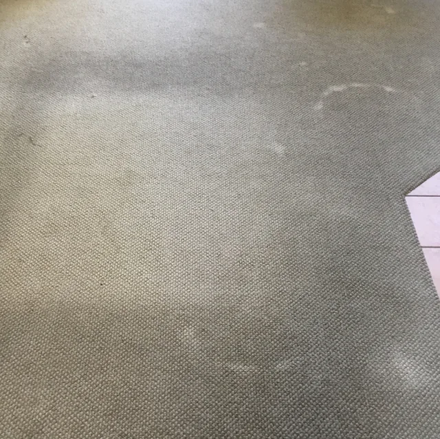 Fitted carpet beside a tile threshold before cleaning: Darker patches and visible spots across the carpet beside a tile edge.