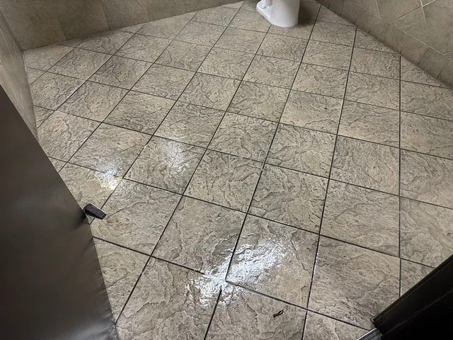 Commercial restroom tile and grout before cleaning: Darkened grout and visible soil on the textured tile by the restroom fixtures.