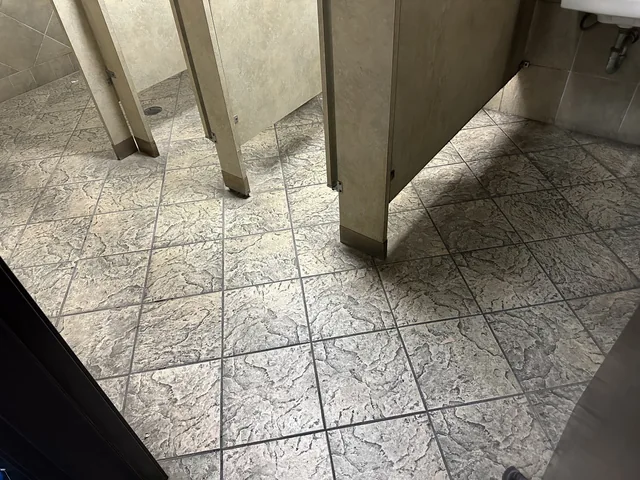 Commercial restroom tile and grout before cleaning: Heavy darkening across the textured tile and grout around restroom partitions.