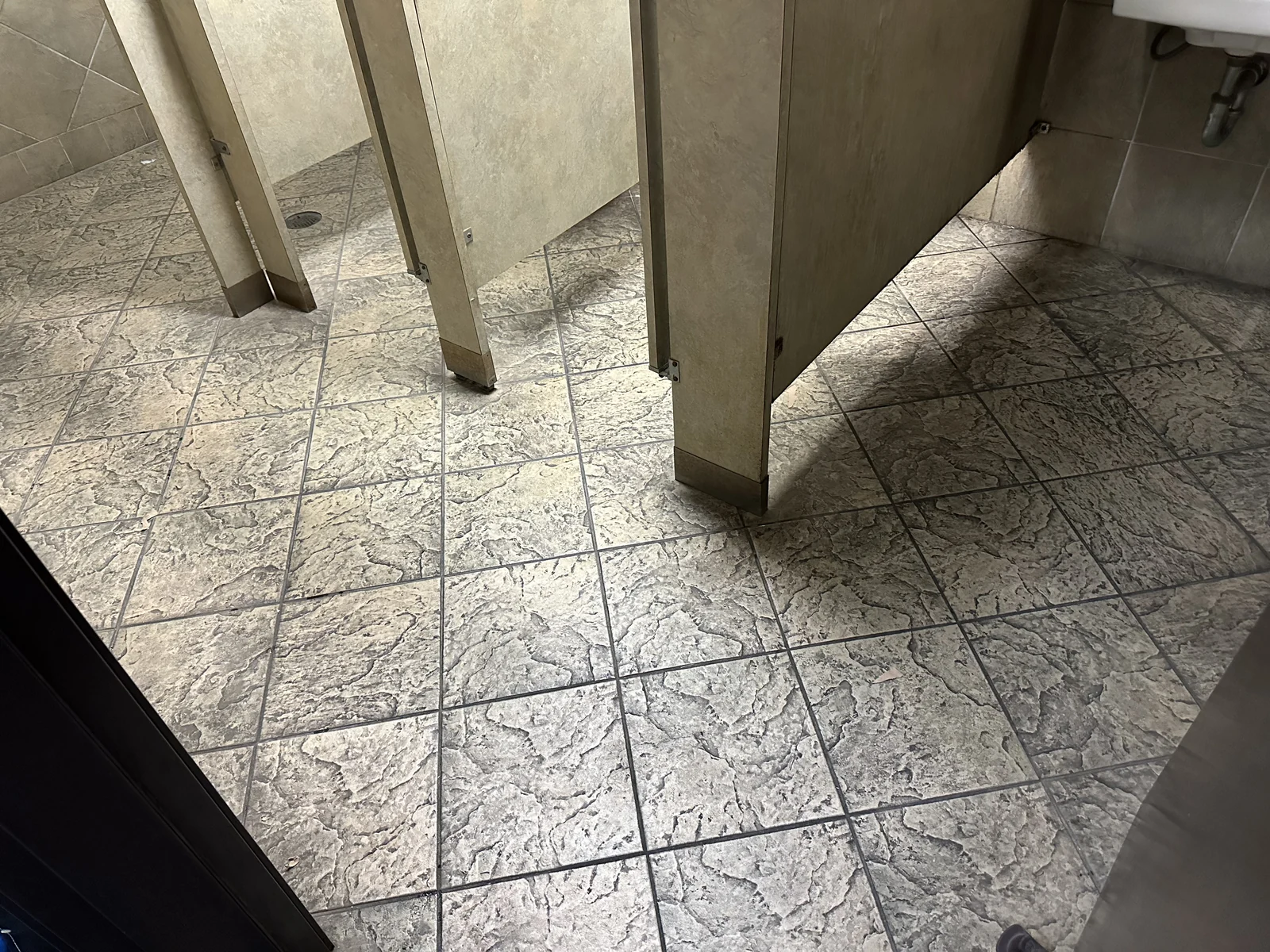 Commercial restroom tile and grout before cleaning: Heavy darkening across the textured tile and grout around restroom partitions.
