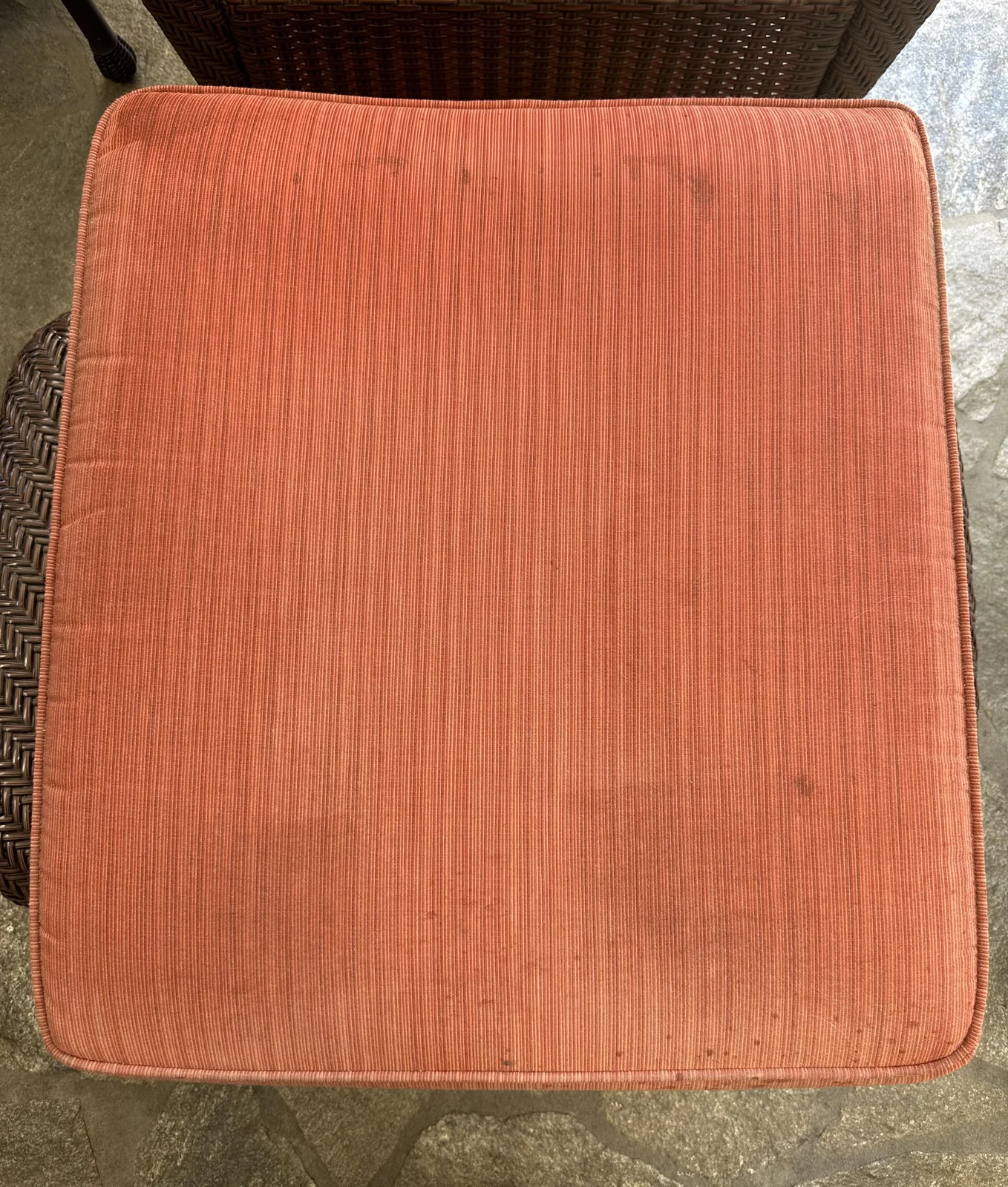 Coral upholstered seat cushion before cleaning: Dark marks scattered across a coral-colored seat cushion.