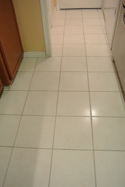 White square kitchen tile and grout after cleaning: The same kitchen walkway with lighter-looking grout around the white tiles.