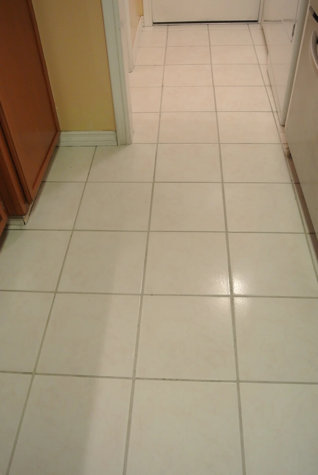 White square kitchen tile and grout after cleaning: The same kitchen walkway with lighter-looking grout around the white tiles.