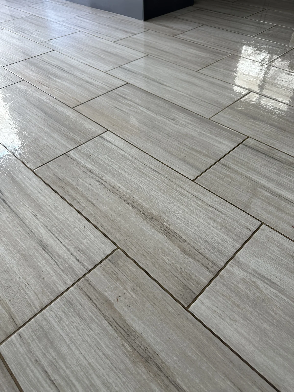 Gray rectangular floor tile and grout before cleaning: Dark joints interrupting the pattern of a gray plank-shaped tile floor.