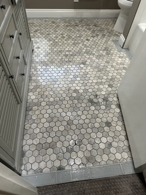 Hexagonal bathroom tile and grout before cleaning: Small hexagonal tiles with darker-looking grout between the vanity and tub.