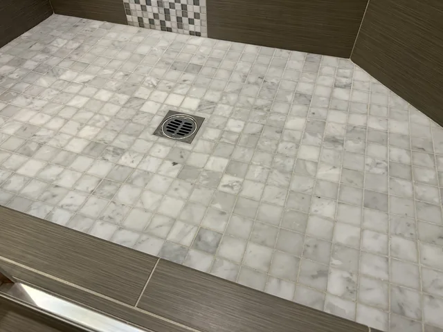 Pale square shower tile and grout after cleaning: The same veined tiles and drain with lighter-looking grout lines.