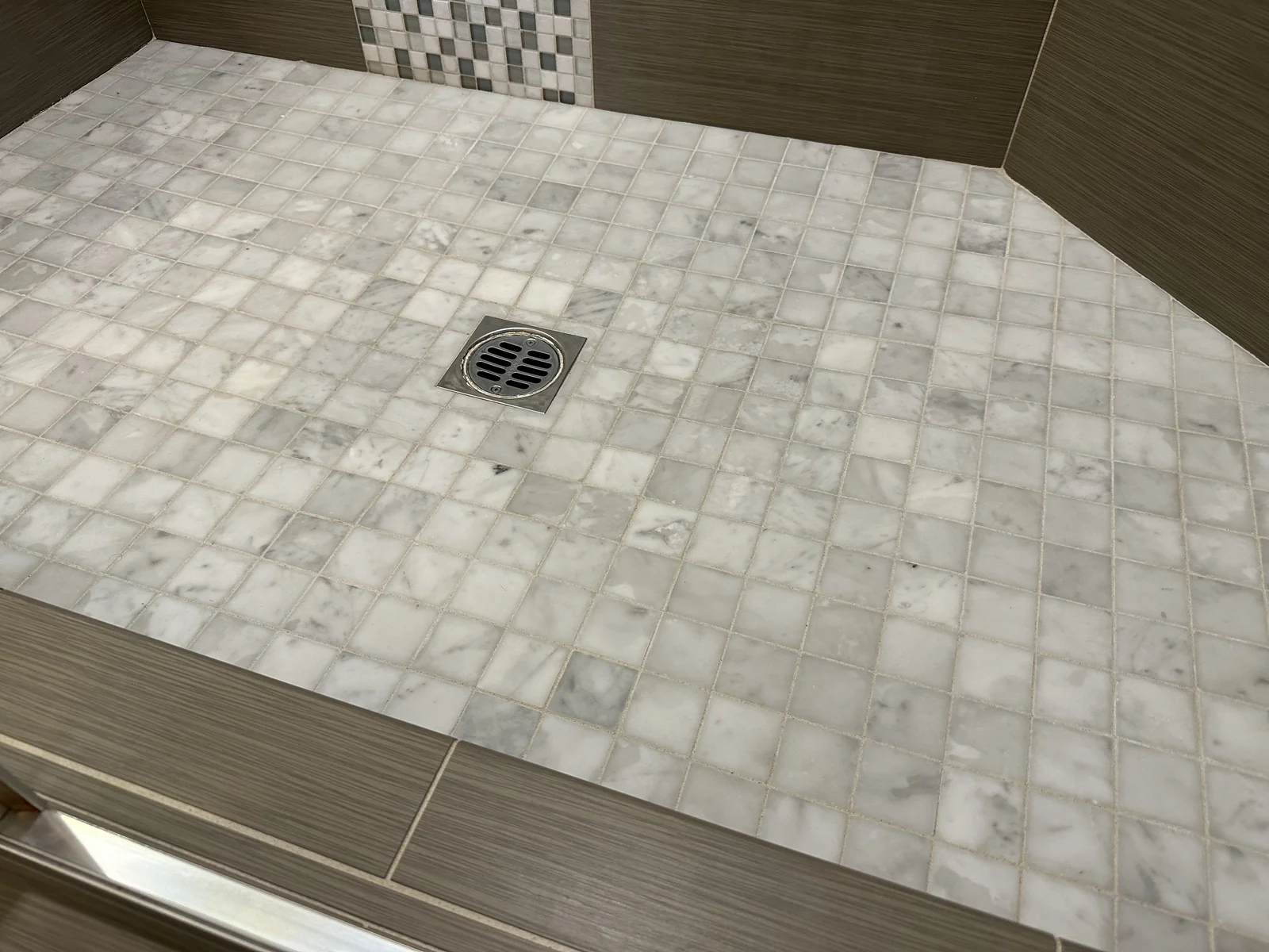 Pale square shower tile and grout after cleaning: The same veined tiles and drain with lighter-looking grout lines.