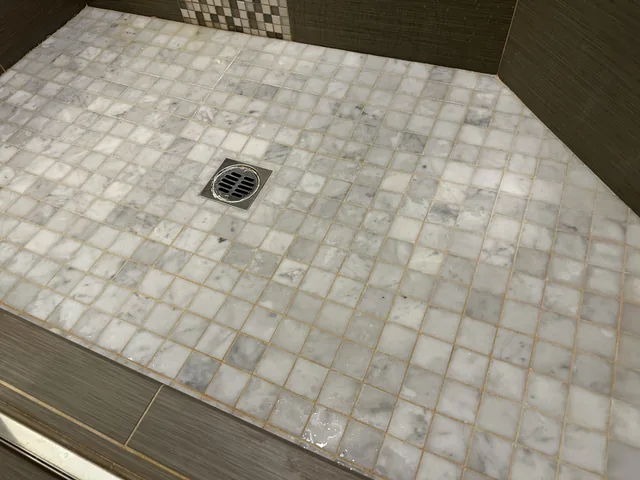 Pale square shower tile and grout before cleaning: Yellowed-looking grout lines across the pale mosaic shower floor.