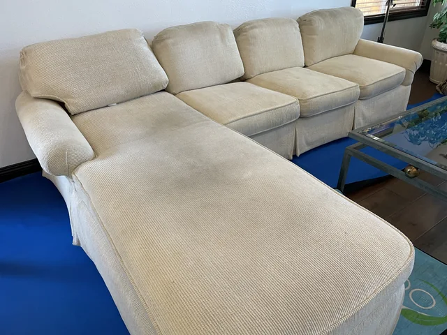 Upholstered sectional before cleaning: Darker patches across the cushions and chaise of a light-colored sectional.