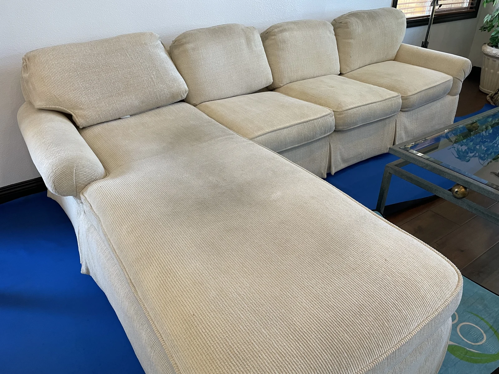 Upholstered sectional before cleaning: Darker patches across the cushions and chaise of a light-colored sectional.