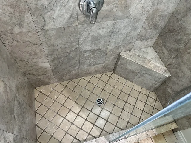 Shower tile and grout after cleaning: A cleaner-looking shower floor, with the matching bench, tile pattern and fixtures in view.