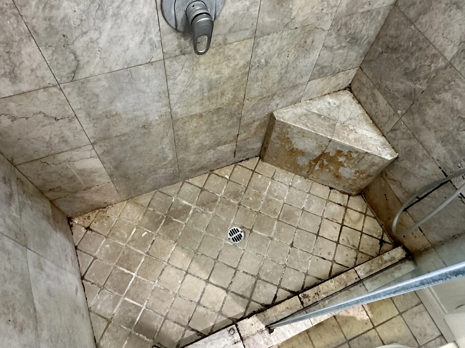 Shower tile and grout before cleaning: Visible discoloration across the shower floor and its grout lines.