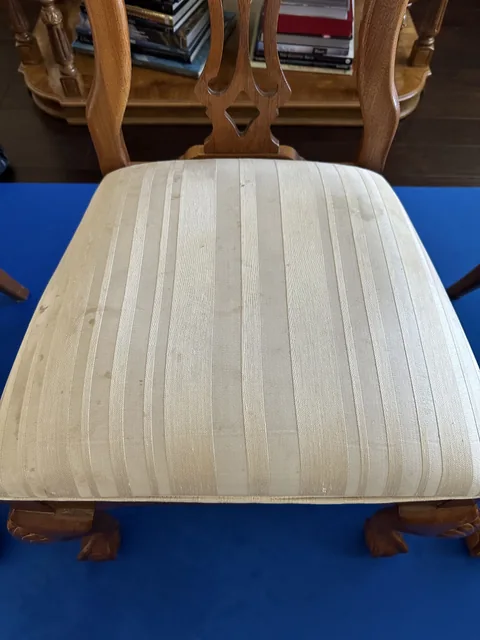 Striped upholstered dining-chair seat before cleaning: Small dark marks on the pale striped upholstery of a dining chair.