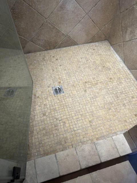 Small square shower tile and grout after cleaning: A more even-looking floor around the same square drain and glass enclosure.