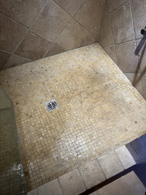 Small square shower tile and grout before cleaning: Uneven discoloration across a mosaic shower floor and its perimeter.