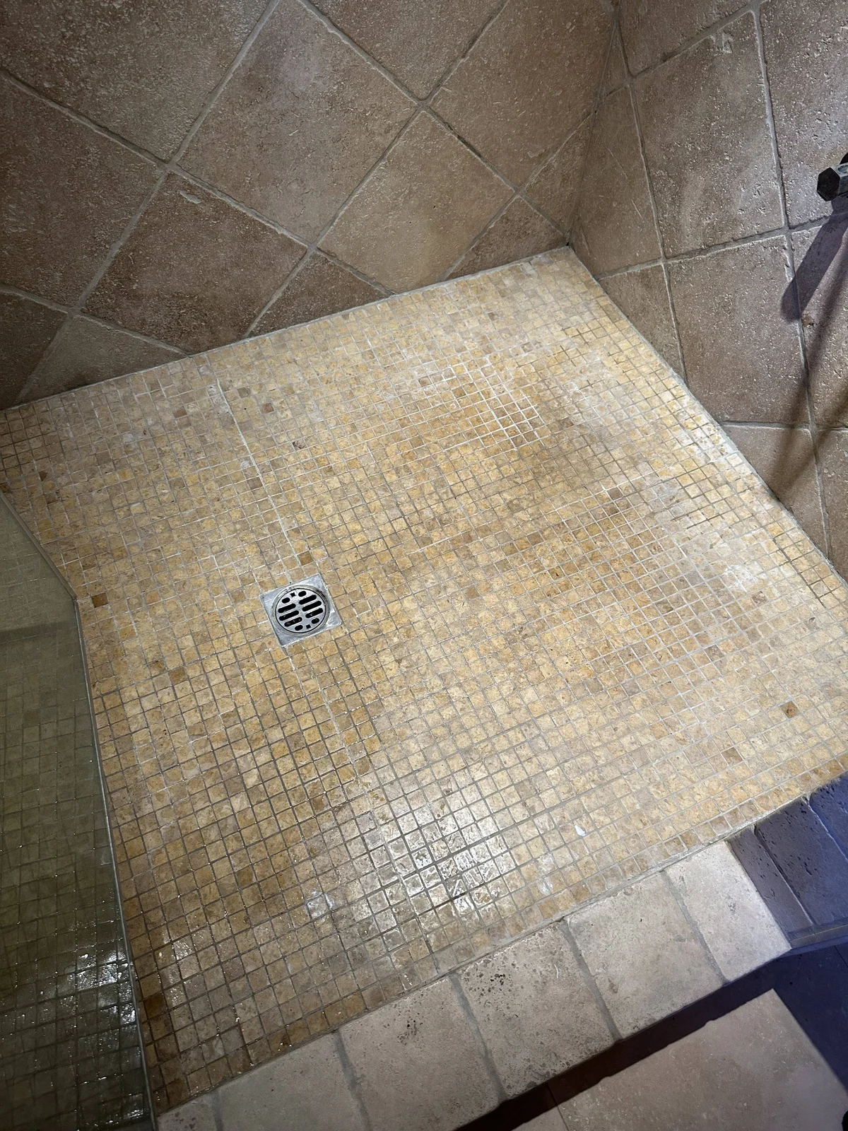 Small square shower tile and grout before cleaning: Uneven discoloration across a mosaic shower floor and its perimeter.