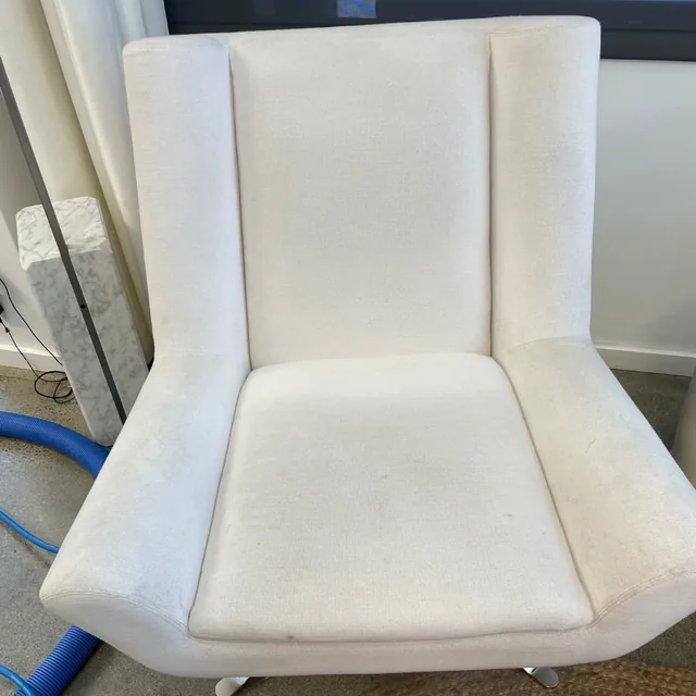 Upholstered accent chair before cleaning: A light-colored chair with visible darkening across the seat and fabric.