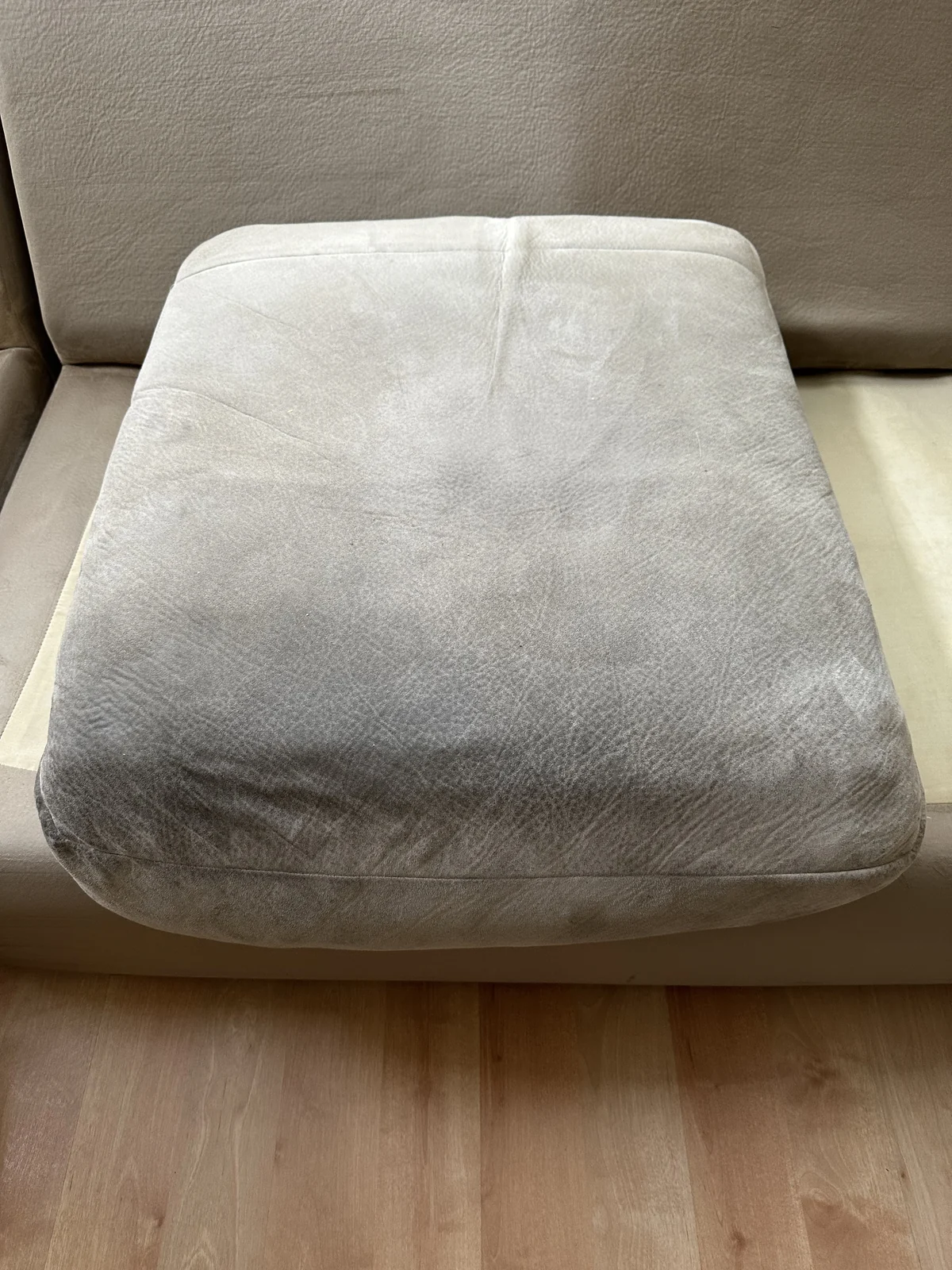 Upholstered ottoman before cleaning: A rounded ottoman with noticeable darkening across its top.