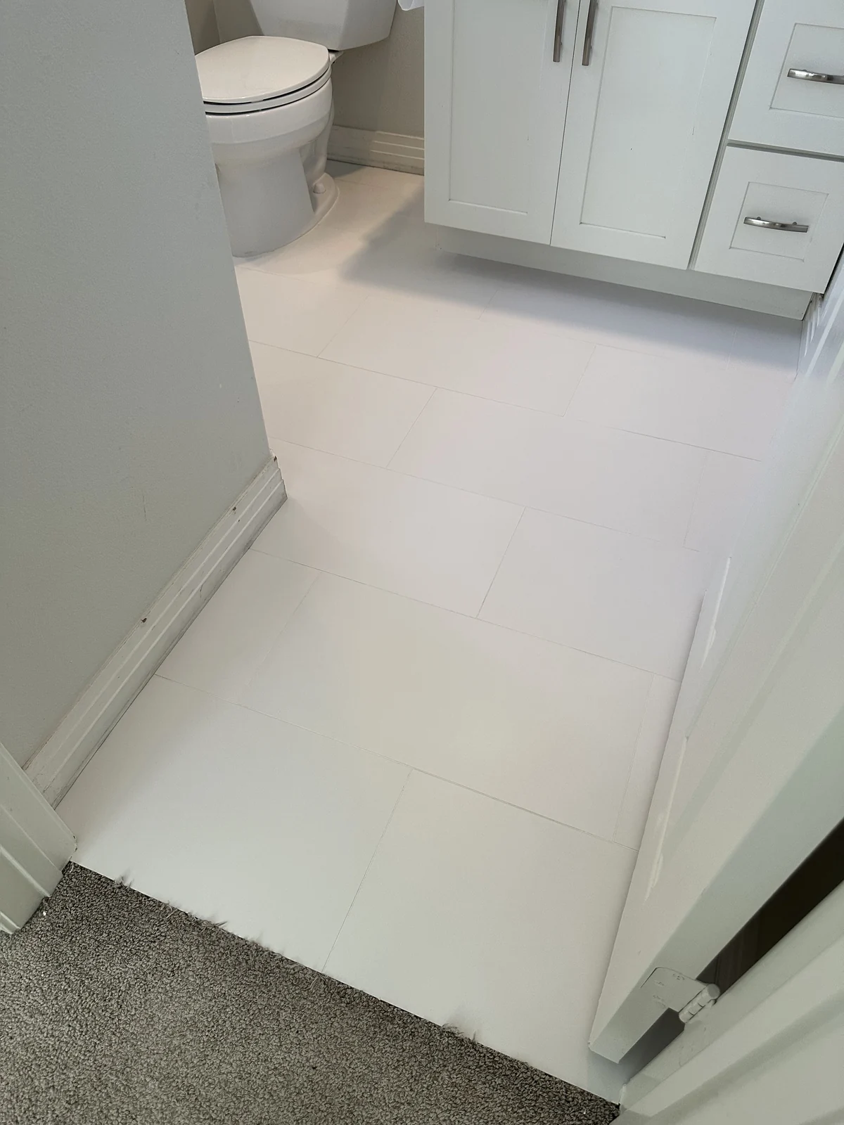 White rectangular bathroom tile and grout after cleaning: Paler-looking grout between the tiles beside the same vanity and toilet.
