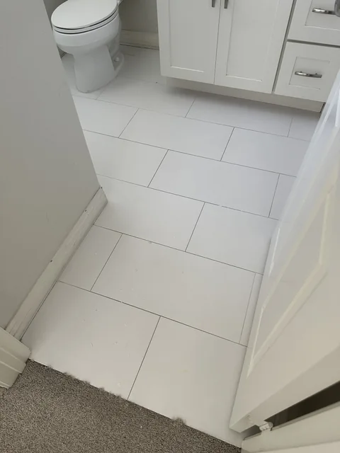 White rectangular bathroom tile and grout before cleaning: Gray grout lines across the white tile at a bathroom entrance.