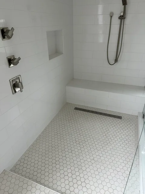Shower wall tile, floor tile and grout before cleaning: A white tiled shower with gray-looking joints across its hexagonal floor.
