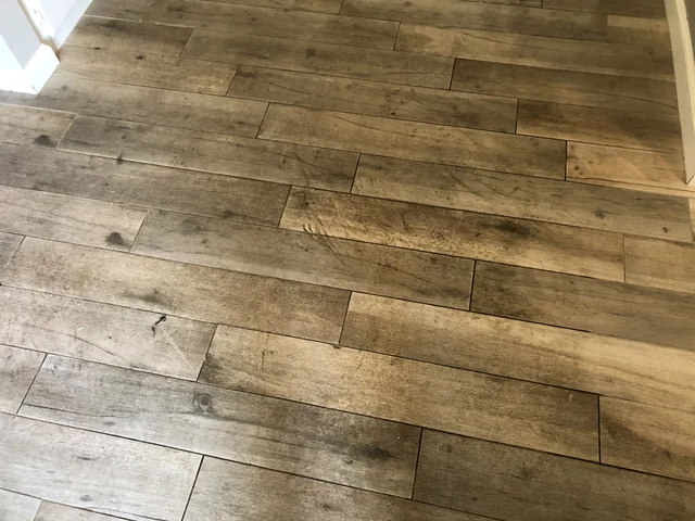 Wood-look tile and grout before cleaning: Darker marks and grout lines across wood-look tile planks.
