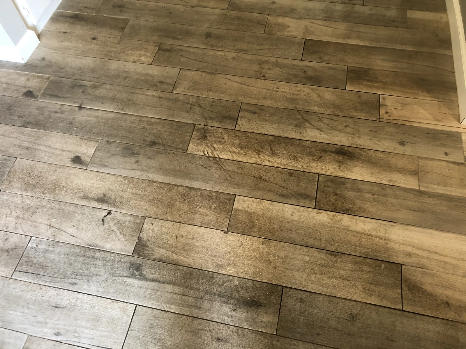 Wood-look tile and grout before cleaning: Darker marks and grout lines across wood-look tile planks.
